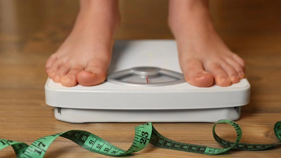 A child stands on weighing scales with a tape measure in front of them