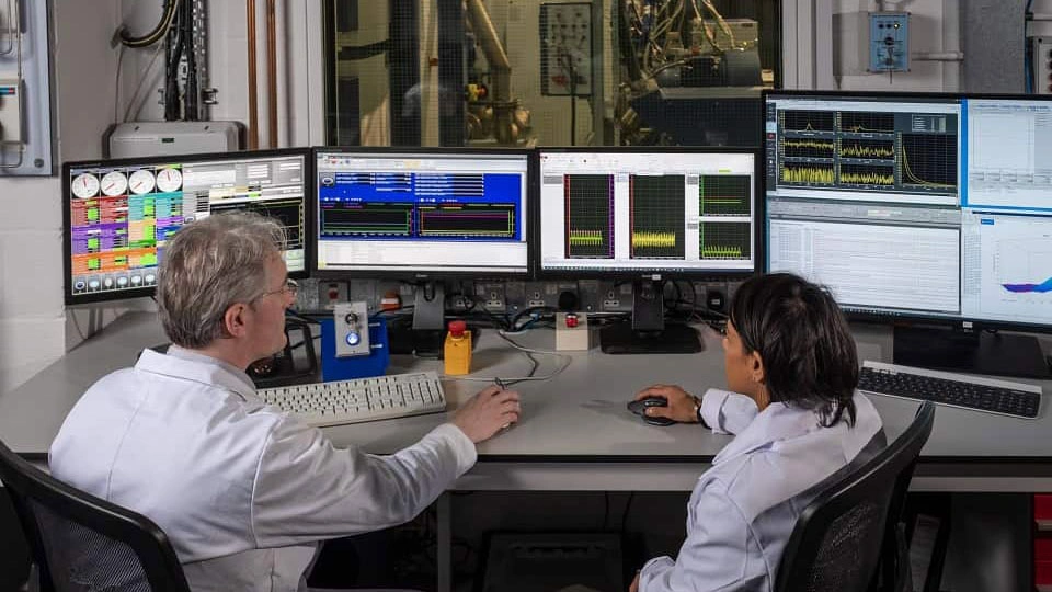 2 researchers at a desk with multiple screens