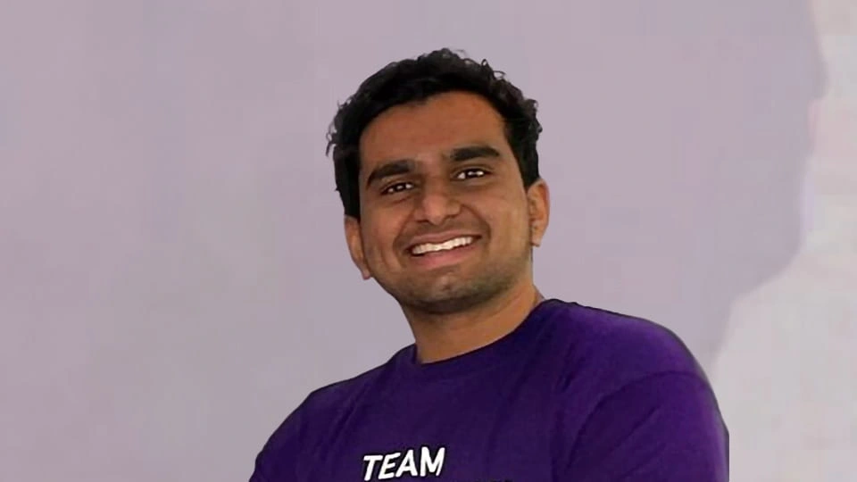 Loughborough Student wears purple welcome to loughborough t-shirt and smiles toward the camera.