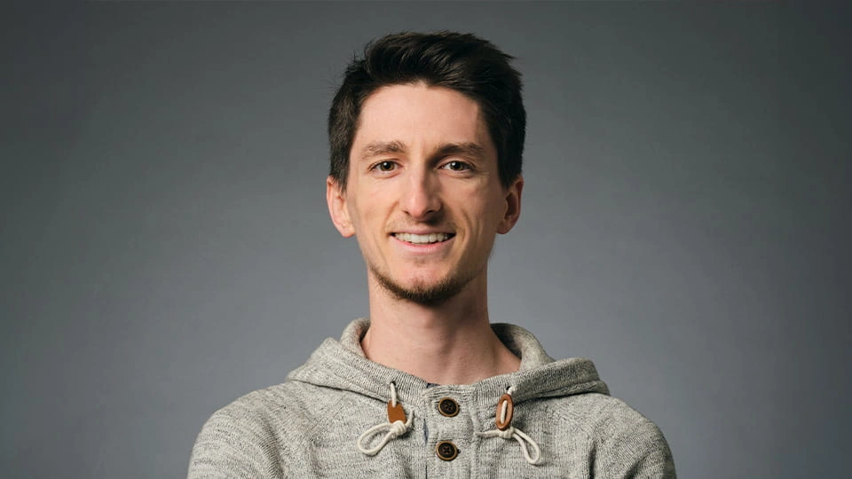 Student smiles to the camera and has a professional soft grey photo background behind him.