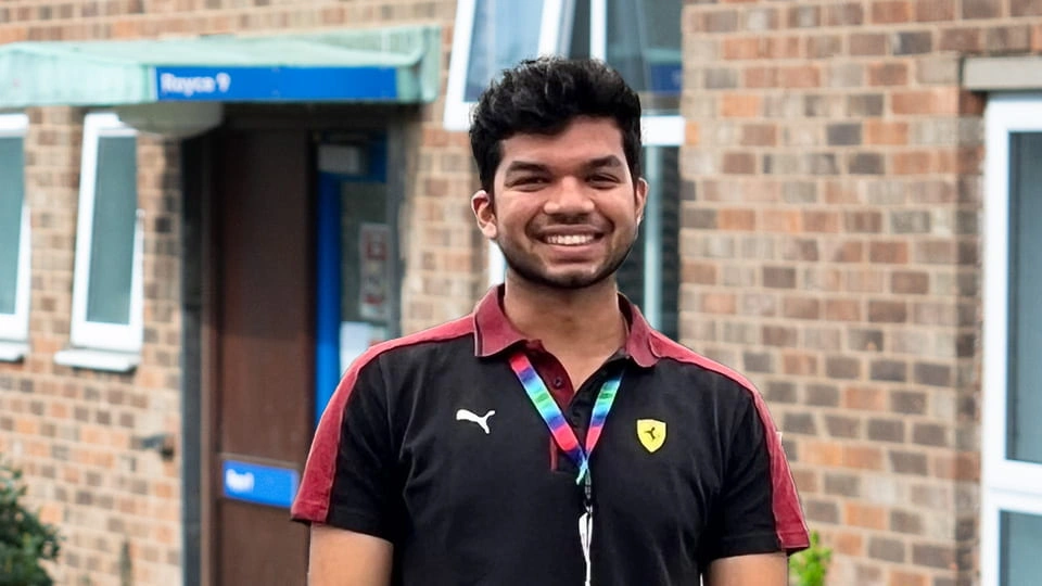 Student is in sports gear and is smiling to the camera, one of the blocks at Royce hall is in the background.