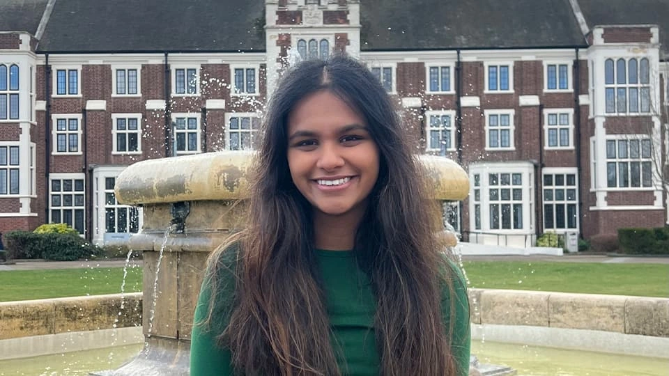 Loughborough University student sits on the iconic fountain outside the university's Hazlerigg building and smiles to the camera.