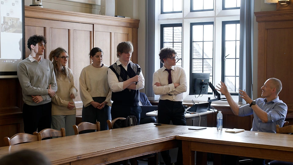 A group of students standing at the front of a large wood panelled room doing a presentation