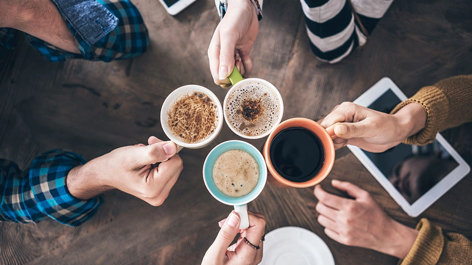 People holding coffee cups over a wooden table