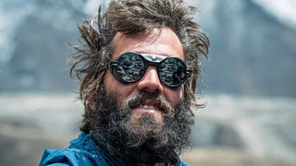 A person with messy hair wearing sunglasses and a blue anorak