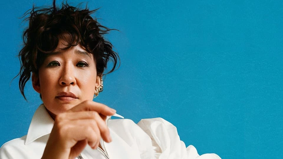 Actress Sandra Oh with a blue background looking directly at the viewer