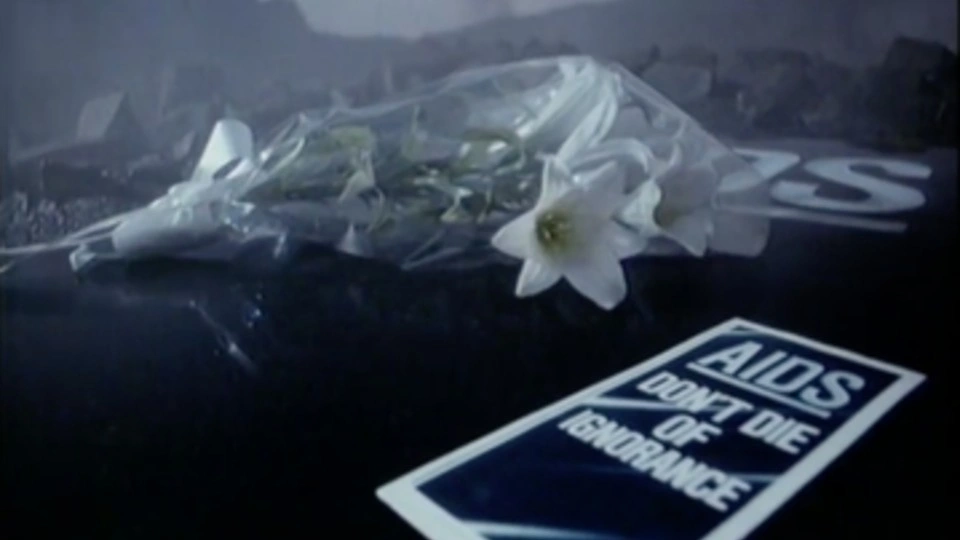 A bunch of flowers alongside a page reading 'AIDS don't die of ignorance'.