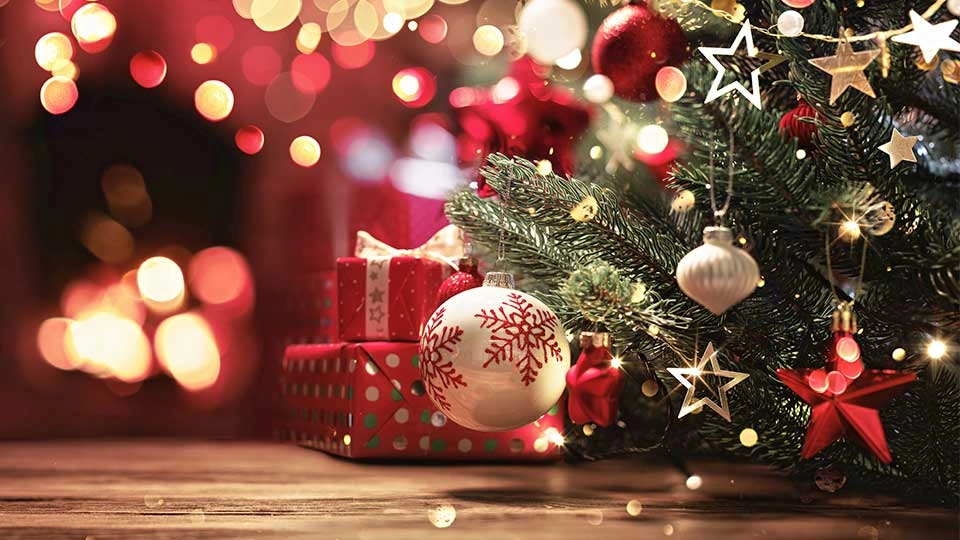 Christmas tree with red and white ornaments, gifts underneath, and warm lights in the background.