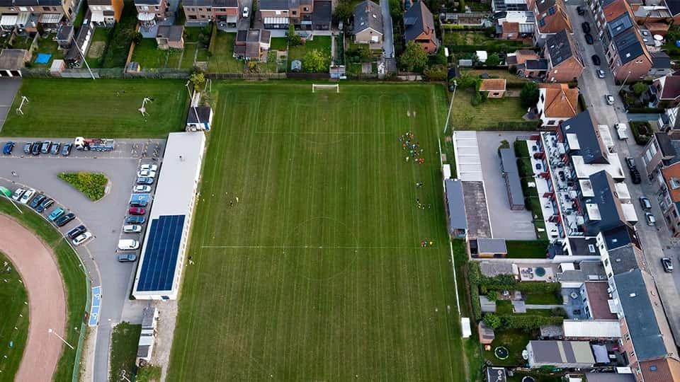 Aerial view of a football pitch with buildings and cars surrounding it.
