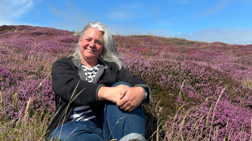 A picture of Jo Bullard sat in a field, smiling at the camera.