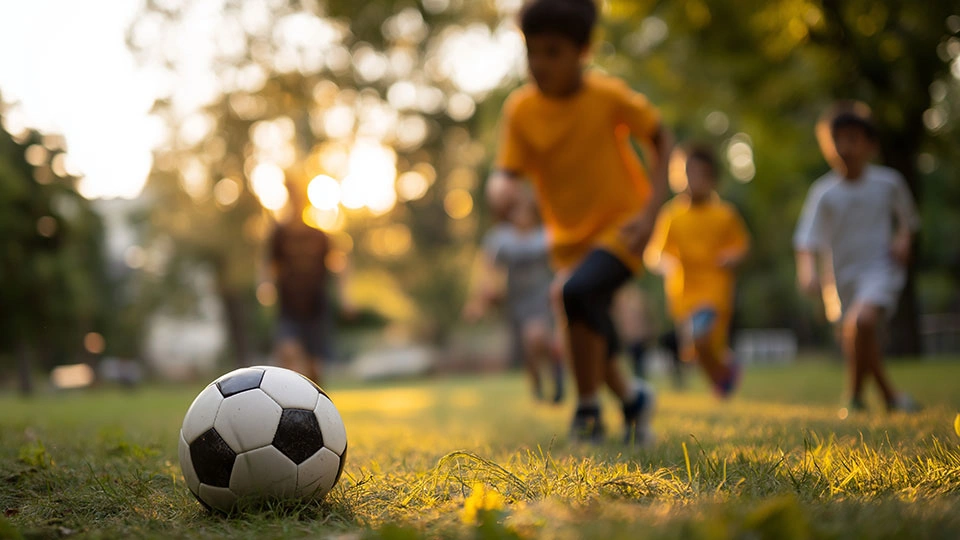 Children running towards a football on a grass field.