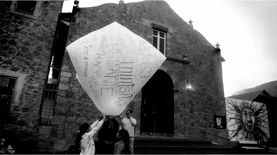 Black and white photo of people holding a large paper lantern outside of a building.