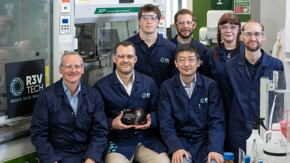 Seven people in a lab wearing R3VTech lab coats and goggles, one holding an award.