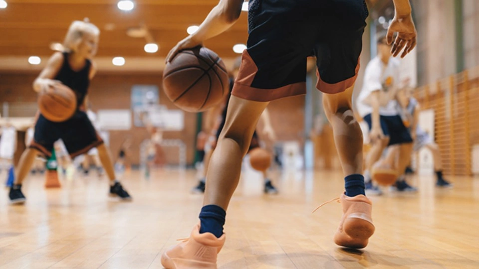 Close-up of young people playing basketball on an indoor court.