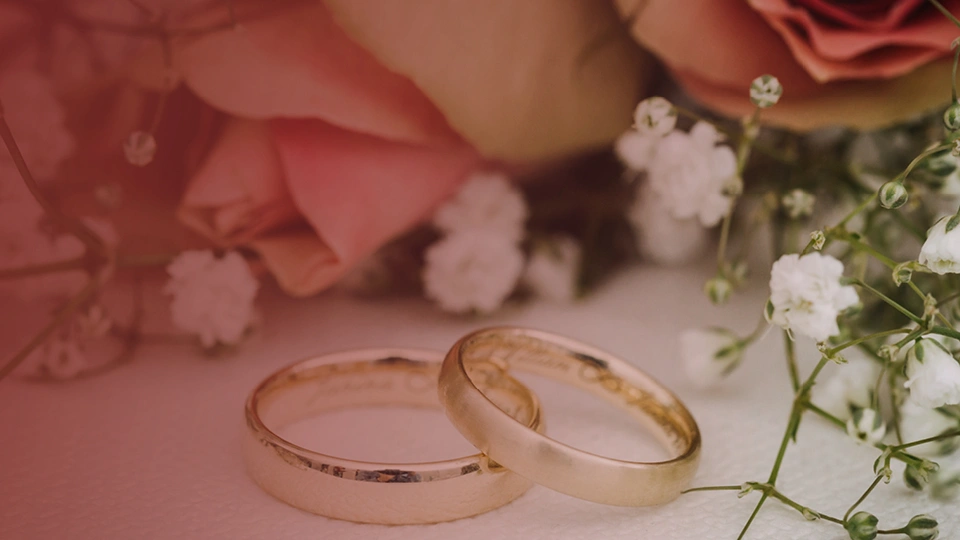 Close-up of two gold rings overlapping on a table with flowers next to them.
