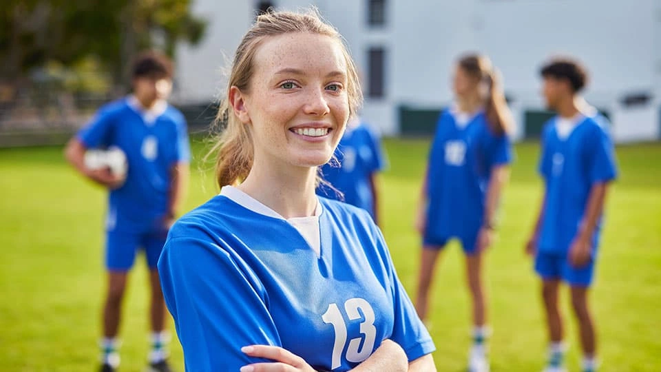 Student athlete smiles in football jersey with other players in background