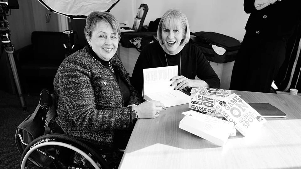 Baroness Grey-Thompson and Sue Anstiss smiling at the camera. There are copies of Sue’s Game On book on the table.