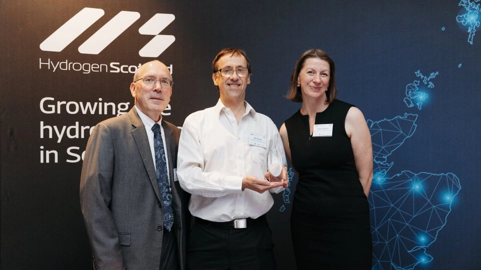 Three people standing together, one holding a trophy.
