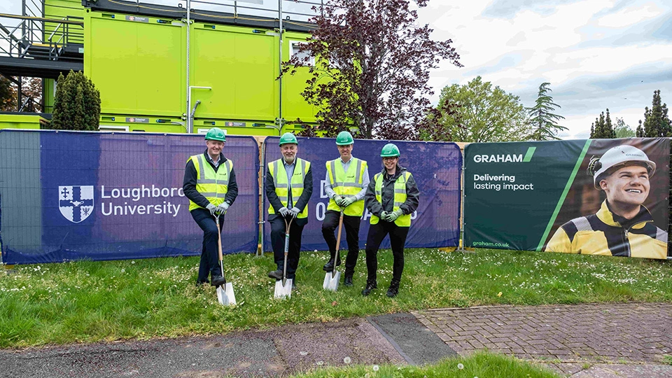 Four people wearing hi-vis jackets and green helmets standing outside of the new student accommodation development on campus.