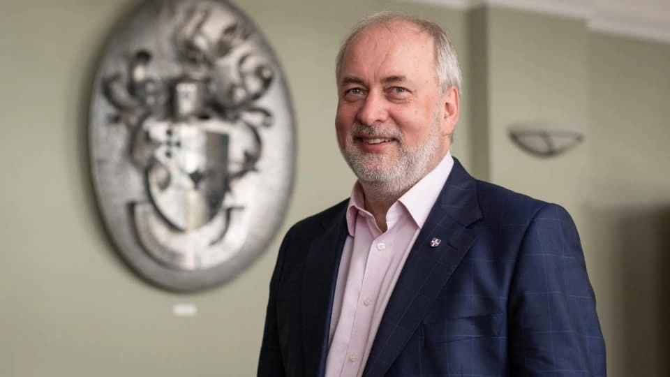 Vice-Chancellor and President Professor Nick Jennings in front of a metal Loughborough University crest