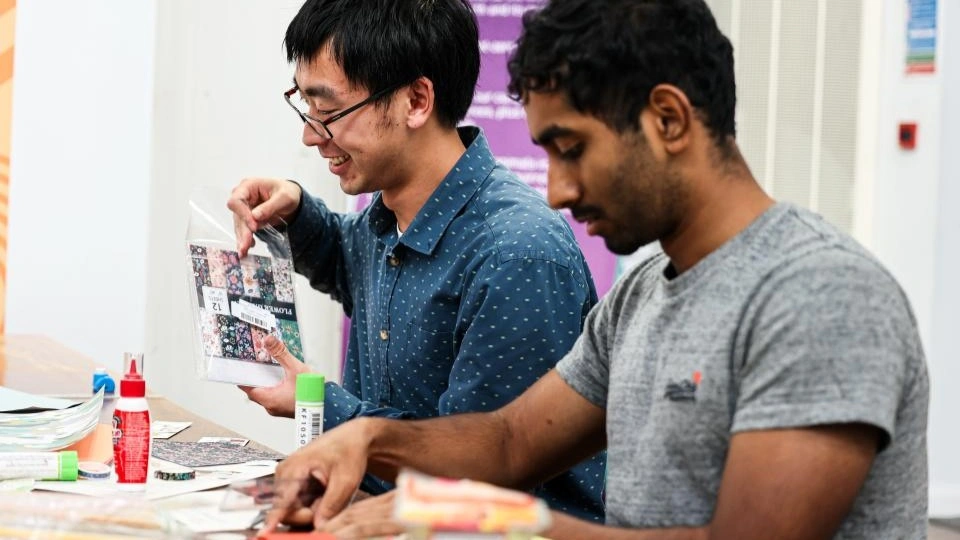 Two people sat down at a table making bookmarks.