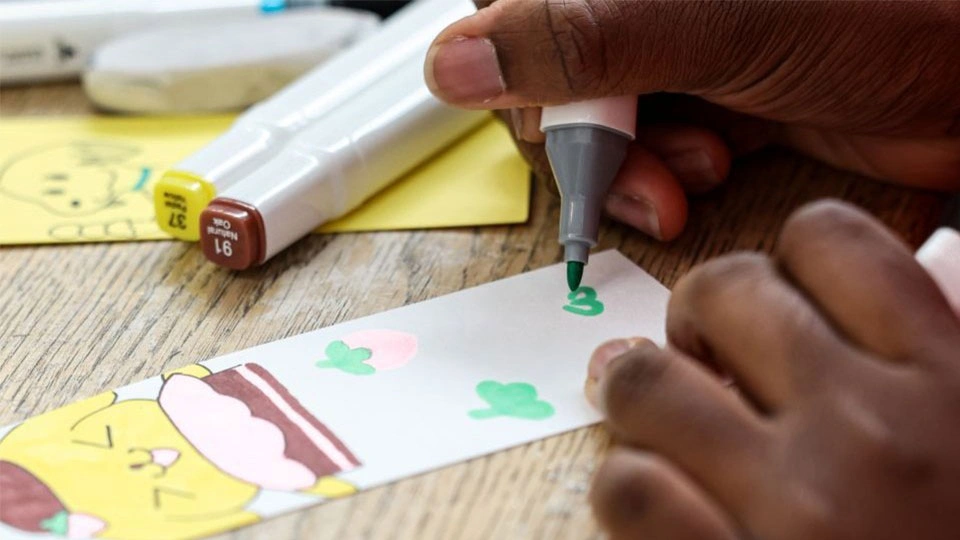 A paper bookmark being decorated with felt pens