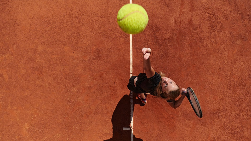 Female tennis player on a clay court serving a ball