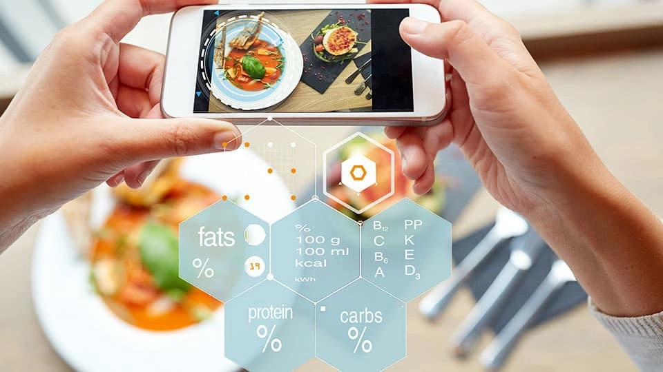 Hands holding a smartphone that scans a meal, displaying nutritional information and food analysis overlays on the screen