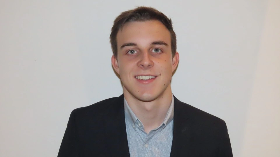 A headshot of Sam Jeffery in a suit