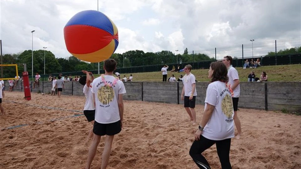 A group of people playing volleyball on a sandy beach, with a ball floating inthe air.