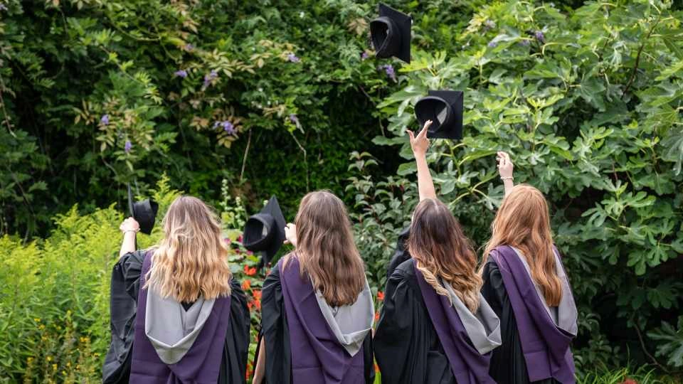 Group of students outdoors wearing graduation gowns throwing their graduation caps into the air. 