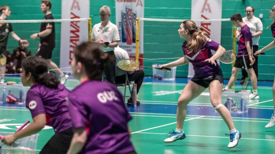 Student playing badminton on an indoor court.