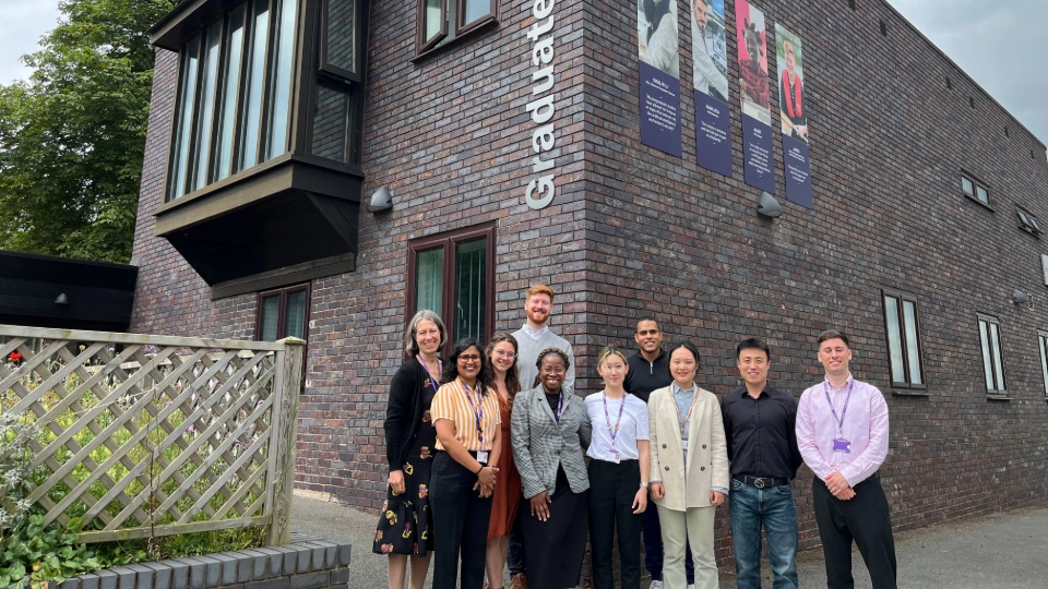 Some Loughborough University doctoral innovation consultants stood beside their supporting staff in front of the Graduate House building