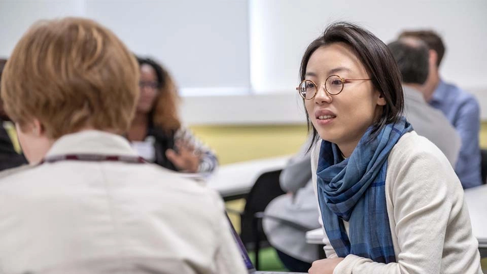 Photo of a woman sitting at a table talking to another person who is facing the opposite way