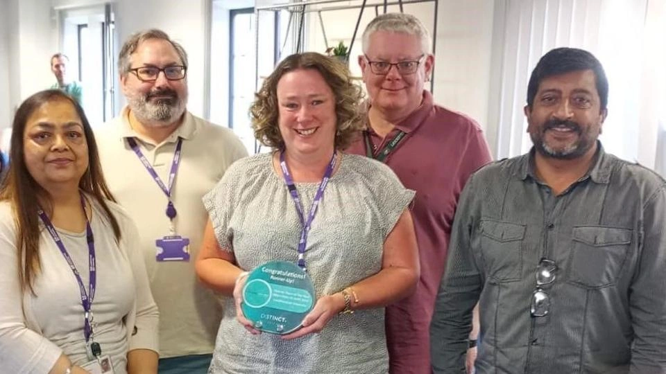 Members of the Loughborough University finance team standing together in a row, smiling and one person is holding the EMFA trophy which reads 'Congratulations! Runner-up!". 