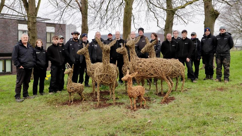 The University Gardens team standing with a group of handcrafted willow deer on campus.