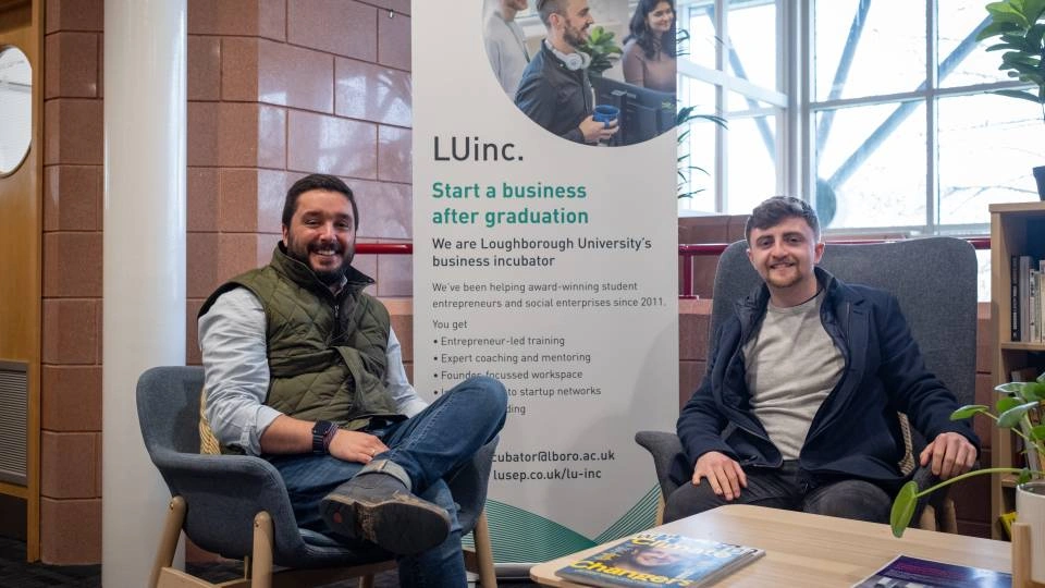 Image of two people sitting and smiling in front of an LUinc. banner. 