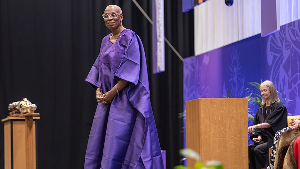 Pauline standing on stage in a purple gown at a graduation ceremony.