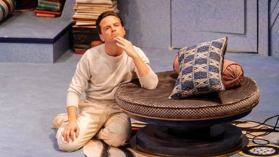 An actor sitting on the floor, resting his arm on a table, looking into the distance