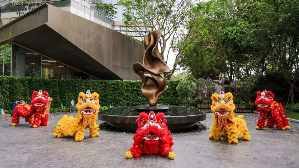 A bronze sculpture in the middle of a fountain surrounded by five red and yellow lion statues.