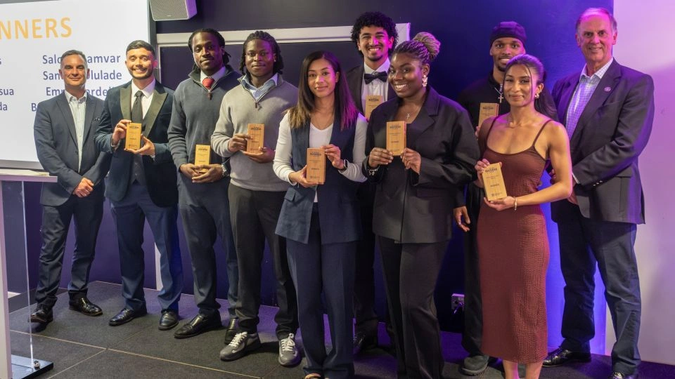 A group of students standing with Professor Sam Grogan and Chris Gill holding trophies.