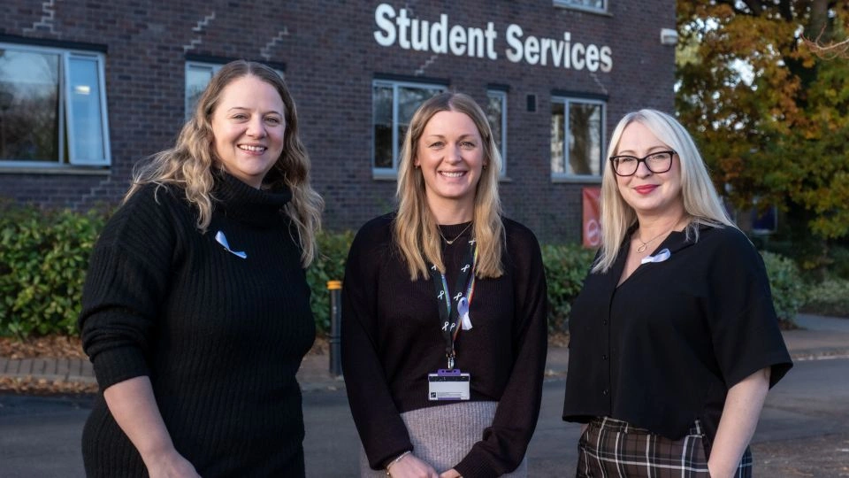 Three members of staff standing in front of the Student Services building wearing white ribbons.