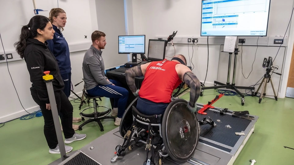 A para athlete in a wheelchair undergoes some testing with three researchers.