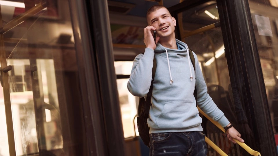 Young man gets off the bus while using his phone to walk and talk