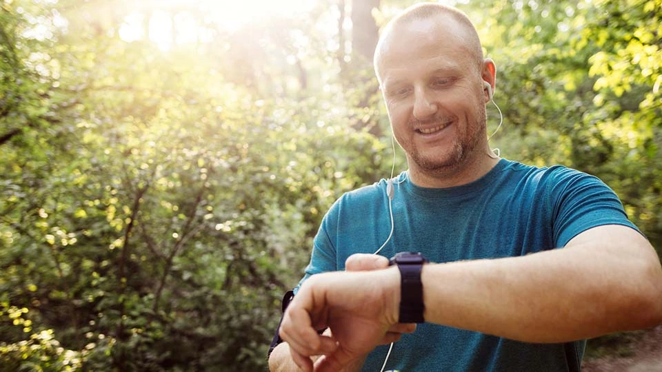 A man checks his fitness tracker while exercising in a forest.