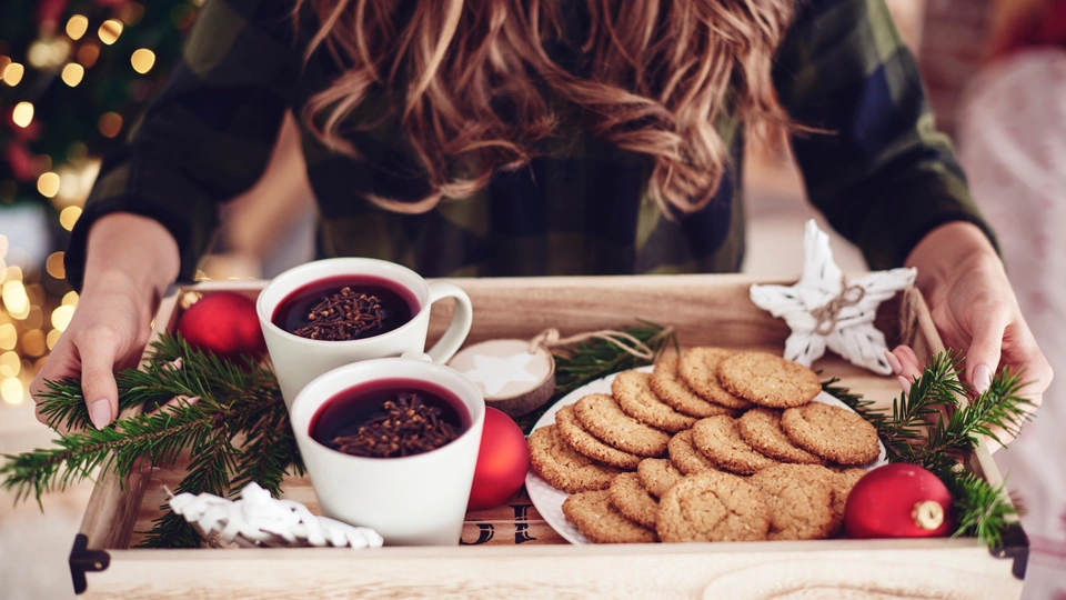 A woman holds a tray with festive cookies and mulled wine