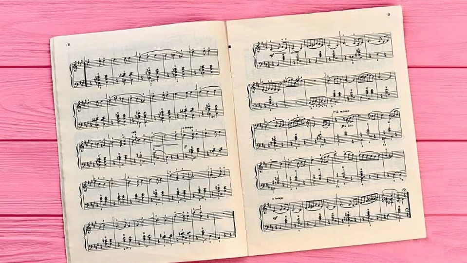 Sheet music booklet open against a bright pink wooden background.