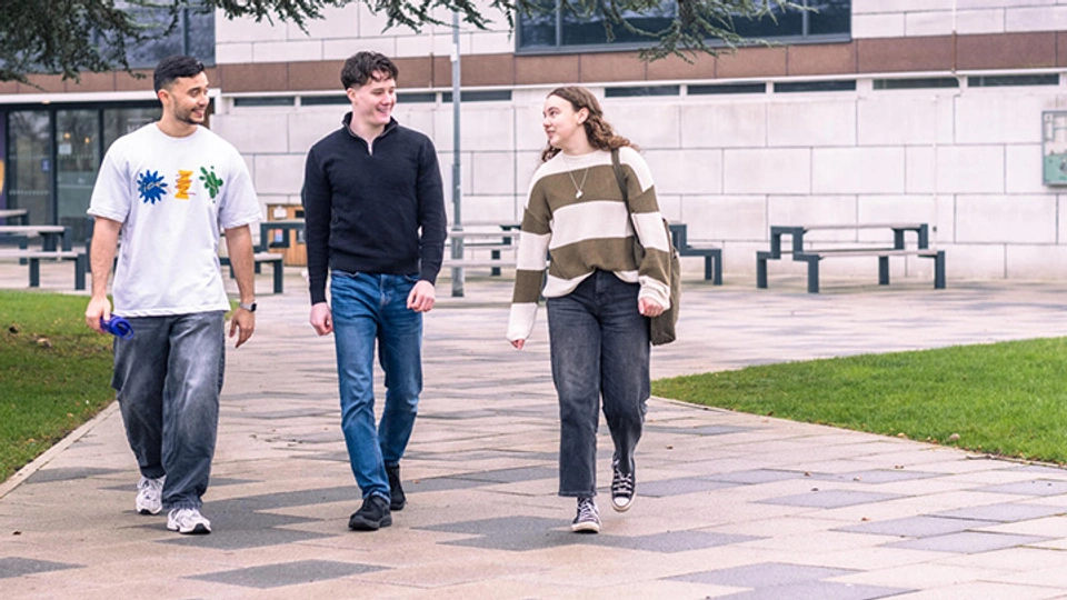 a group of three students chatting as they walk through campus