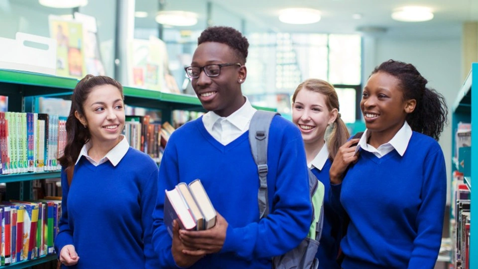 A school boy and three school girls laugh and walk together