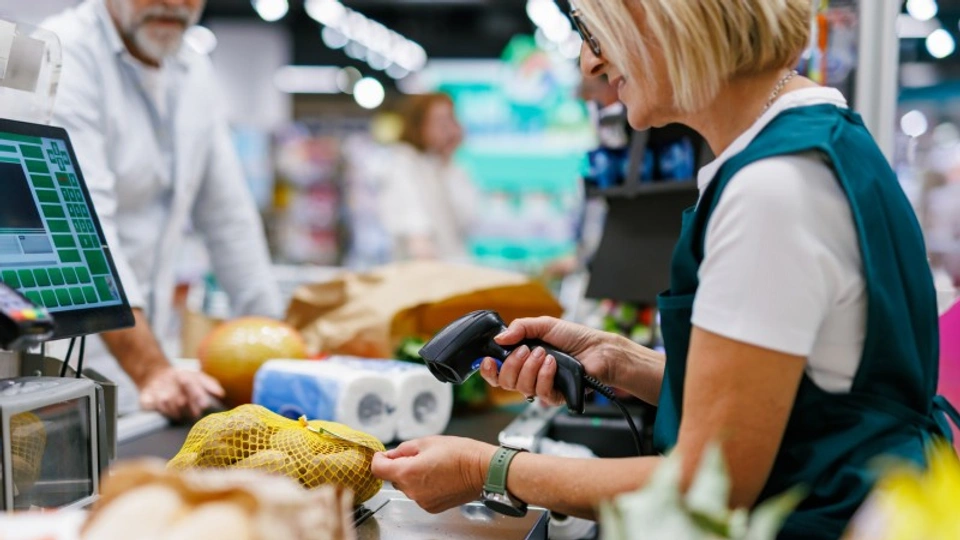 A man stands at a check queue in a supermarket while the cashier scans his lemons